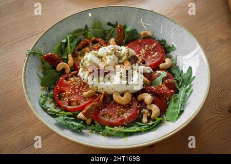 Primo piano di sana insalata italiana con pomodori secchi e freschi, mozzarella, rucola, anacardi, sesamo e pesto di basilico. Fotografia alimentare per sito web. Foto Stock