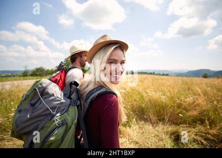 Donna escursionista che sbatte e cammina in campo con un uomo, natura all'aperto. Sport, libertà, concetto di vacanza. Coppia innamorata. Scatto del punto di vista. Foto Stock