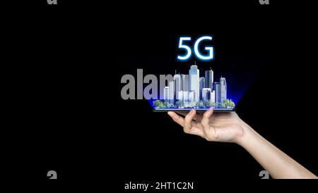 Mano che tiene un telefono con una città intelligente 5G sullo sfondo. Il concetto di rete 5G, Internet mobile ad alta velocità, reti di nuova generazione. Foto Stock