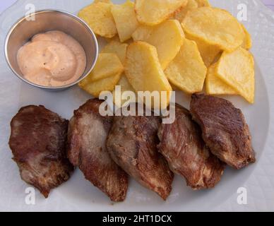 Bistecca di controfiletto alla griglia con patate a fette arrostite, il tutto su un piatto bianco. Una ciotola con salsa calda. Cucina spagnola. Foto Stock