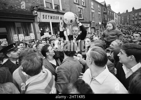 Il tradizionale Royal Shrovetide Football Match, una partita di "calcio medievale" giocata ogni anno il martedì di Shrove e il mercoledì delle ceneri nella città di Ashbourne nel Derbyshire.ospite d'onore Sir Stanley Matthews è portato in alto spalla dagli abitanti del villaggio attraverso la strada principale verso il punto di partenza del gioco. 22nd febbraio 1966. Foto Stock