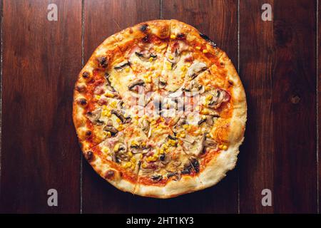 Primo piano della pizza a base di pomodoro, formaggio, pancetta, mais dolce e funghi. Foto Stock