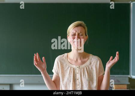 Arrabbiato frustrato insegnante di scuola con le sue mani in piedi di fronte a una lavagna in una classe Foto Stock