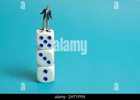 Fotografia di personaggi giocattolo in miniatura. Un uomo d'affari che si sta levando in piedi sopra i dadi bianchi. Isolato su sfondo blu. Foto immagine Foto Stock