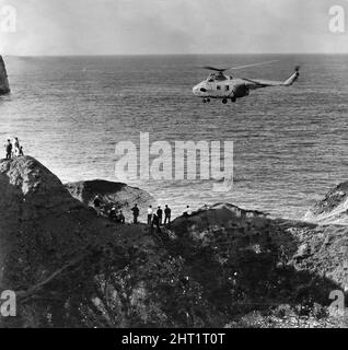 I villeggianti guardano come un viticoltori della RAF aiuta la parte infortunata a bordo di un elicottero Westland Whirlwind HAR10 mentre si aggira sulle scogliere di Flamborough. 30th agosto 1965 Foto Stock