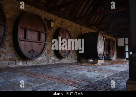 Fila di botti di legno in un muro di pietra accanto alla porta del vino tedesca in Schweigen-Rechtenbach, al confine con la Germania francese, all'estremità meridionale del Th Foto Stock