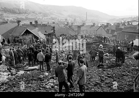 Aberfan, South Wales, circa 21st ottobre 1966 Foto mostra il fango e la devastazione causati quando la miniera di petrolio dalla collina sopra la città dietro è venuto giù e inghiottito la scuola junior Pantglas il 21st ottobre 1966. Soccorritori cercando di trovare vittime e aiuto, monista il fango e macerie intorno al sito della scuola. Il disastro di Aberfan è stato un crollo catastrofico di una punta di petrolio collirica nel villaggio gallese di Aberfan, vicino a Merthyr Tydfil. È stato causato da un accumulo di acqua nella roccia accumulata e scisto, che improvvisamente ha iniziato a scivolare in discesa sotto forma di slurry e ha inghiottito il Foto Stock