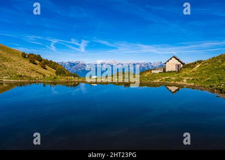 Vista su un laghetto in cima al Monte Cesen fino alle colline meridionali delle Dolomiti. Foto Stock