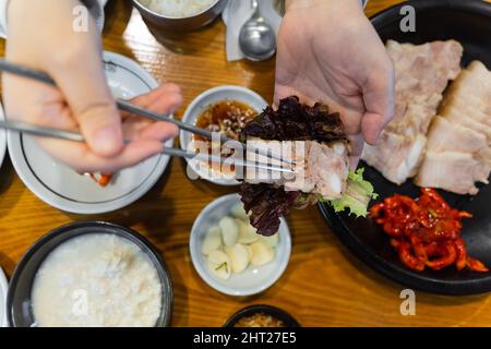 Mettere la carne e i gamberi salati sulla lattuga con le bacchette per fare il bossam. Il Bossam è un piatto di maiale bollito in cucina coreana. Foto Stock
