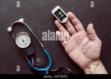 Pulsossimetro utilizzato per misurare la frequenza del polso e il livello di ossigeno nel sangue per il paziente su braccio maschio, sfondo scuro Foto Stock