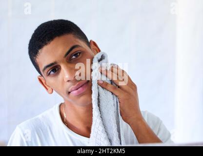 Una routine di cura della pelle del mattino è altrettanto importante per una notte. Scatto corto di un bel giovane uomo con un asciugamano per strofinare il viso la mattina alle Foto Stock