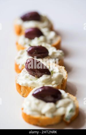 Molti pezzettini di pane con tzatziki spalmati e frutta in linea su sfondo bianco, primo piano. Foto Stock