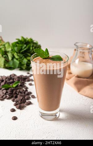 milkshake proteico al cioccolato in vetro bianco fondo cucina. deliziosa porzione milkshake al cioccolato. agitare proteico sano su latte vegano Foto Stock