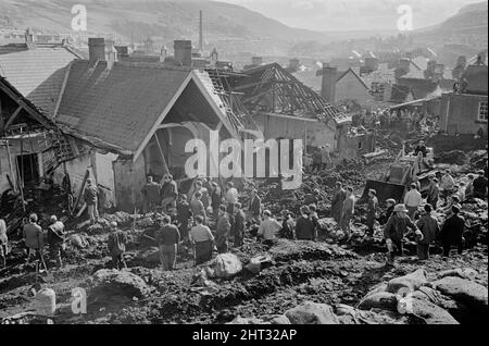 Aberfan, South Wales, circa 21st ottobre 1966 Foto mostra il fango e la devastazione causati quando la miniera di petrolio dalla collina sopra la città dietro è venuto giù e inghiottito la scuola junior Pantglas il 21st ottobre 1966. Soccorritori cercando di trovare vittime e aiuto, monista il fango e macerie intorno al sito della scuola. Il disastro di Aberfan è stato un crollo catastrofico di una punta di petrolio collirica nel villaggio gallese di Aberfan, vicino a Merthyr Tydfil. È stato causato da un accumulo di acqua nella roccia accumulata e scisto, che improvvisamente ha iniziato a scivolare in discesa sotto forma di slurry e ha inghiottito il Foto Stock