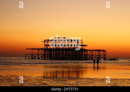 Vista al tramonto con bassa marea del molo ovest di Brighton, con sagome e riflessi. Foto Stock