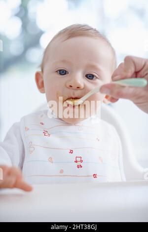 Disordinato e adorabile. Immagine ritagliata di un bambino nutrito dalla madre. Foto Stock