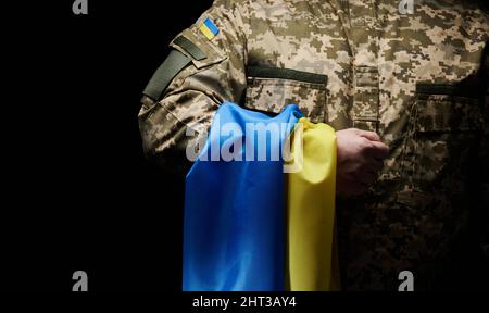 Il soldato ucraino detiene una bandiera dello stato indipendente dell'Ucraina. Fermezza e coraggio del popolo nella lotta contro gli invasori. Unbroke Foto Stock