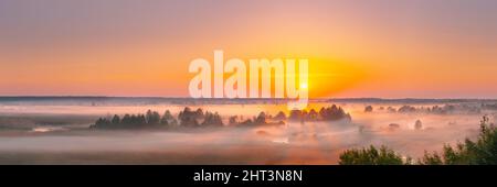 Incredibile tramonto all'alba sul paesaggio mistico. Vista panoramica del cielo mattutino di Foggy con il Sol Levante sopra la Foresta Misty e il Fiume. Inizio Estate natura di Foto Stock