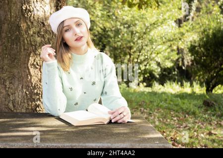 Giovane femmina in un berretto che legge un libro in un parco Foto Stock