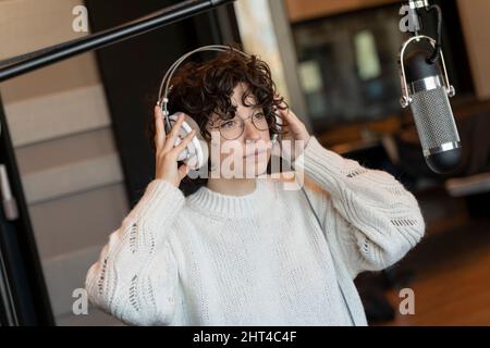 Una giovane cantante di capelli ricci con occhiali che registrano una canzone in un vero studio Foto Stock