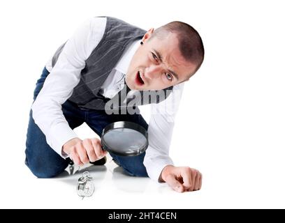 Fatica a tenere traccia del tempo. Un giovane puzzled che guarda un piccolo orologio attraverso una lente d'ingrandimento. Foto Stock