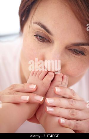 Baciare quei piedi piccoli. Immagine di primo piano ritagliata di una madre che bacia i piedi delle sue bambine. Foto Stock