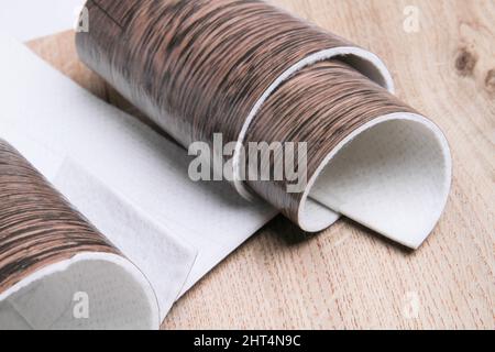Linoleum. Rotolo di linoleum su sfondo nero. Rivestimenti per pavimenti. Posa di rivestimenti per pavimenti. Tessitura di legno su un rotolo. Il campione viene arrotolato. Foto Stock