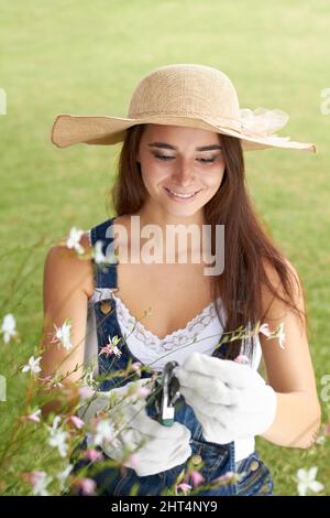Mantenendo il suo giardino nella forma superiore della punta. Una giovane donna attraente che tende al suo giardino. Foto Stock