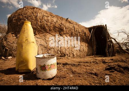 Un rifugio Maasai e una tazza di stagno e un contenitore d'acqua. Questa zona di conservazione permette l'abitazione umana, a differenza di altri in Tanzania. Zona di Ndutu, Ngorongoro Co Foto Stock