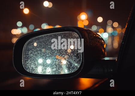 rorse sullo specchietto retrovisore per auto ad ala di sera. Luci notturne in città Foto Stock