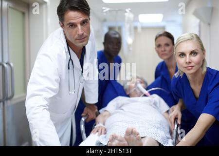 Portandola alla SALA OPERATORIA. Ritratto di un gruppo di medici che spingono un paziente verso il basso nella sala. Foto Stock
