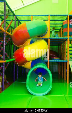 Ragazzo seduto in fondo a uno scivolo di tunnel di un parco giochi al coperto nel parco Frajda Foto Stock