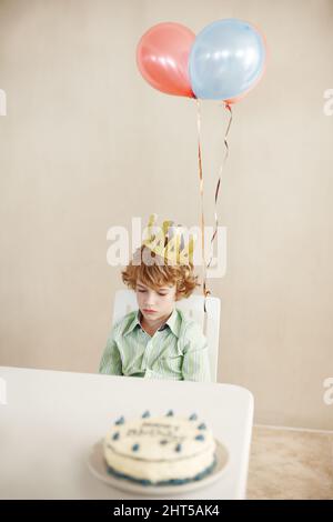 Forse tutti hanno dimenticato il mio compleanno. Scatto di un ragazzino carino che sembra infelice mentre si siede a un tavolo con la sua torta di compleanno. Foto Stock