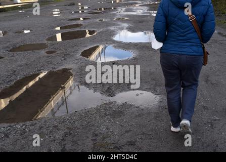 Una donna cammina davanti a una serie di pozzanghere a seguito di una tempesta di pioggia a Vancouver, British Columbia, Canada Foto Stock