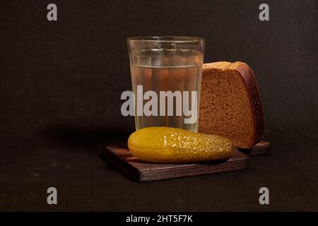 Un bicchiere sfaccettato di vodka, pane di segale e cetriolo sottaceto su un piedistallo di legno Foto Stock