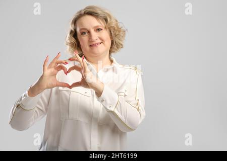 Donna anziana felice mostra gesto d'amore. Donna di mezza età ha piegato le palme delle sue mani a forma di cuore. Foto Stock