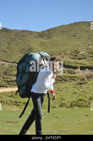 Un allegro giovane turista maschio a piedi con trasporto zaino Parachute in montagna Foto Stock