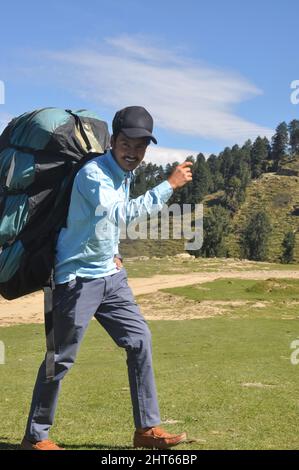 L'intera lunghezza di un ragazzo sorridente, guardando la macchina fotografica mentre cammina con il trasporto zaino paracadute in montagna Foto Stock
