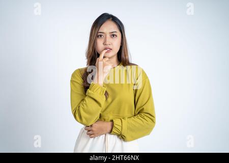 Giovane donna asiatica che pensa qualcosa con il gesto del morso del dito Foto Stock