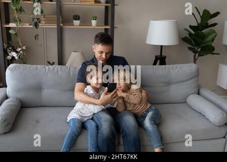 Affettuoso padre amorevole e bambini piccoli usando il cellulare a casa. Foto Stock