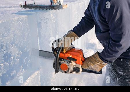 Realizzare sculture di ghiaccio. Un uomo taglia la superficie in un blocco di ghiaccio con una sega a benzina sul lago Baikal. Foto Stock