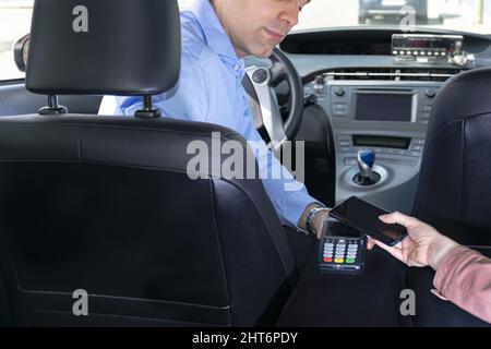 Passeggero che paga il tassista tramite la macchina POS con il suo telefono Foto Stock