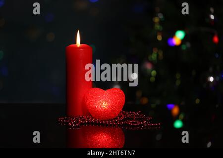 Primo piano di una candela rossa e cuore decorativo con un albero di Natale illuminato sullo sfondo Foto Stock