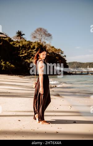Scatto a corpo pieno di una giovane donna tedesca che indossa un abito estivo nero su una spiaggia sabbiosa in Thailandia Foto Stock