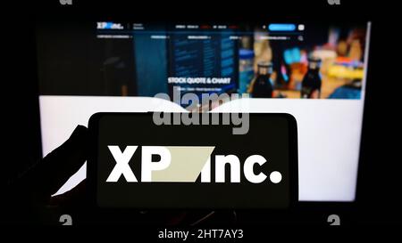 Persona che tiene il cellulare con il logo della società di investimento brasiliana XP Inc. Sullo schermo di fronte al sito web aziendale. Mettere a fuoco sul display del telefono. Foto Stock