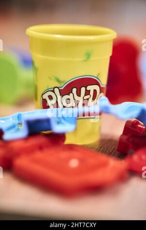 Colpo verticale di una vasca di argilla Play-Doh accanto ai giocattoli di plastica su uno sfondo sfocato Foto Stock