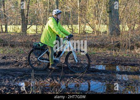 Donna di oltre cinquanta anni fa un giro in bicicletta con la sua e-bike lungo un percorso fangoso e attraverso le pozzanghere, Lueneburg, bassa Sassonia, Germania Foto Stock