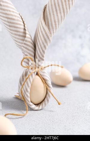 Primo piano del coniglietto pasquale fatto da ovoassorbente e biancheria a strisce. Le uova di Pasqua sono beige chiaro su sfondo grigio chiaro. Tendenza di decorazione tradizionale Foto Stock