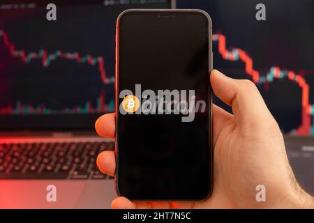 Bitcoin BTC app di criptovaluta analisi del mercato azionario sullo schermo del telefono cellulare in mani di uomo e downtrend grafici di negoziazione dati sullo sfondo, febbraio 2022, San Francisco, USA. Foto Stock