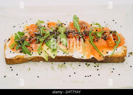 Toast al salmone affumicato, formaggio fresco, avocado e rucola Foto Stock